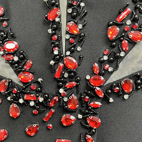 Close-up of a decorative fabric with red and black gemstones on a gray background