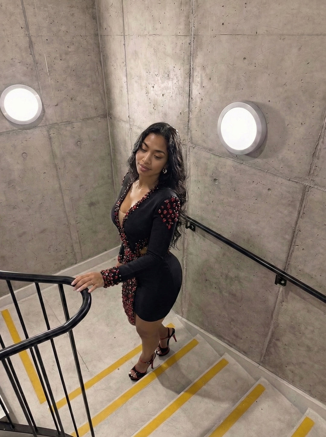Woman in a black dress standing on a staircase with concrete walls and yellow stripes.
